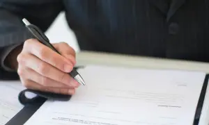 Dłoń w garniturze pisze długopisem na dokumencie. Czy to autentyczny podpis, czy próba podrobienia podpisu?