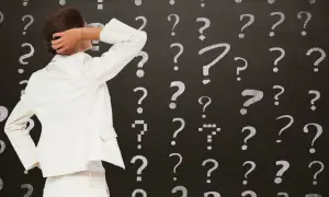 Kobieta w białym garniturze drapie się po głowie na tle tablicy z pytajnikami. Czy to decyzja o wydziedziczeniu?