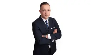 Mężczyzna w garniturze ze skrzyżowanymi rękami na białym tle.