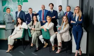 Grupa profesjonalistów w garniturach pozuje do zdjęcia w nowoczesnym biurze.