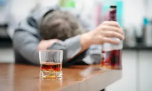 Ubezwłasnowolnienie alkoholika. Mężczyzna w garniturze leży na blacie, obok szklanka z whisky i butelka.