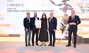 Pięć osób w strojach formalnych pozuje do zdjęcia na tle sceny z grafiką i napisem "I MIEJSCE".