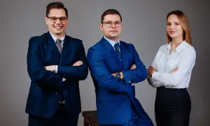 Trzy osoby w garniturach i białej koszuli, stojące z rękami skrzyżowanymi na piersiach.