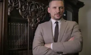 Mężczyzna w garniturze stoi przed regałem z książkami.