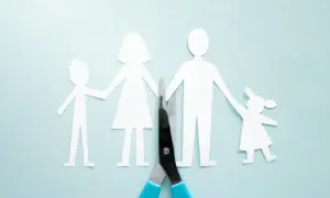 Rodzina z papieru rozdzielona nożyczkami. Dzieci trzymają się za ręce rodziców, symbolizując opiekę nad dzieckiem po rozwodzie.