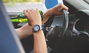 Ręce na kierownicy, jedna trzyma butelkę piwa. Ryzykowne zachowanie, stan po użyciu alkoholu.