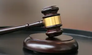 Drewniany młotek sędziowski ze złotym pierścieniem na czarnej powierzchni.