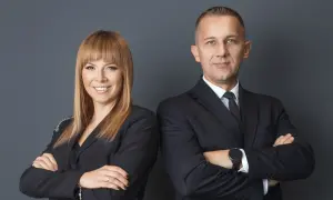 Dwoje prawników w czarnych garniturach, stojących obok siebie ze skrzyżowanymi rękami.