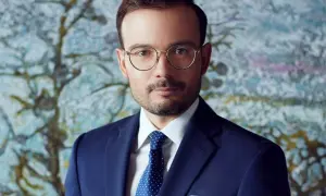 Mężczyzna w okularach i granatowym garniturze na tle abstrakcyjnego obrazu.