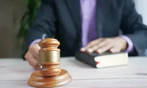 Sędzia kładzie rękę na księdze podczas rozprawy sądowej. Obok stoi drewniany młotek.
