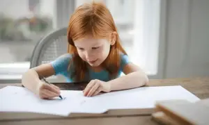 Ruda dziewczynka z zapałem rysuje, co jest przykładem nauczania indywidualnego w domu.