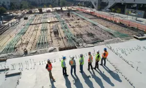 Grupa budowlańców w kaskach i kamizelkach omawia postęp prac na budowie. W tle widać zbrojenie i instalacje, zgodne z art. 62 prawa budowlanego.
