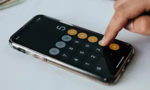 Dłoń wpisuje liczby na kalkulatorze w telefonie. Obliczenia mogą dotyczyć darowizny a zachowek.
