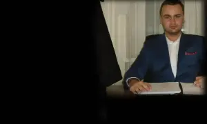 Mężczyzna w niebieskiej marynarce siedzi przy biurku z dokumentami.