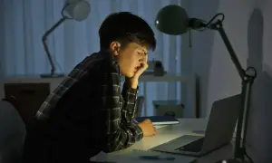 Chłopiec przy biurku, zrezygnowany, zmęczony. Czyżby padł ofiarą cyberprzemocy?