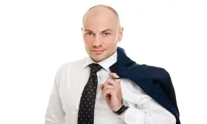 Łysy mężczyzna w białej koszuli i krawacie, z marynarką na ramieniu.