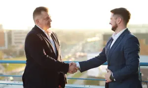 Dwóch mężczyzn w garniturach ściska sobie dłonie na tle miasta.