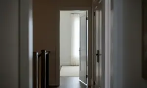 Korytarz z otwartymi drzwiami, sugerującymi naruszenie miru domowego. W tle jasne zasłony i dywan.
