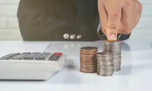 Ręka układa monety na stosie, obok kalkulatora. Zastanawiasz się, ile kosztuje sprawa o zasiedzenie u adwokata?