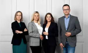 Cztery osoby w strojach biznesowych stoją obok siebie na jasnym tle.