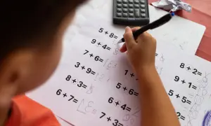Dziecko rozwiązuje zadania matematyczne, które mogą być częścią dyskalkulia testu. Widoczny jest arkusz z działaniami i kalkulator.