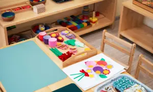 Zestaw do tworzenia kwiatów metodą Montessori: kolorowe papierowe foremki, listki, kółka i wstążki na drewnianej tacy.