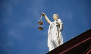 Posąg Temidy z wagą i mieczem na tle błękitnego nieba.