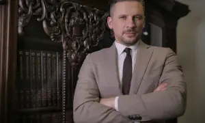 Mężczyzna w garniturze stoi przed regałem z książkami.