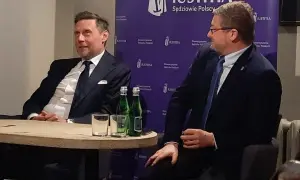 Dwóch mężczyzn w garniturach siedzi przy stole, za nimi fioletowe tło z logo "JUSTITIA".