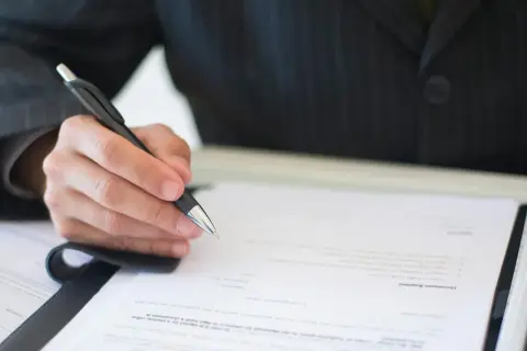 Dłoń w garniturze pisze długopisem na dokumencie. Czy to autentyczny podpis, czy próba podrobienia podpisu?