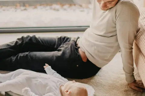 Mężczyzna patrzy na dziecko leżące na dywanie. Czy to jego syn? Zaprzeczenie ojcostwa wisi w powietrzu.