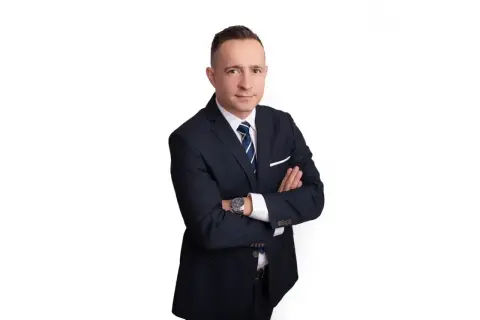 Mężczyzna w garniturze ze skrzyżowanymi rękami na białym tle.
