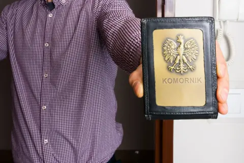 Mężczyzna w koszuli prezentuje legitymację z orłem i napisem "KOMORNIK". Może to oznaczać egzekucję komorniczą.