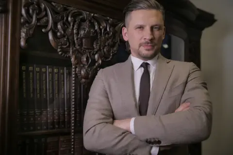 Mężczyzna w garniturze stoi przed regałem z książkami.