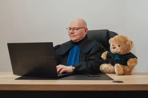Sędzia z pluszowym misiem przy laptopie. Zastanawiasz się, ile kosztuje porada prawna u notariusza?