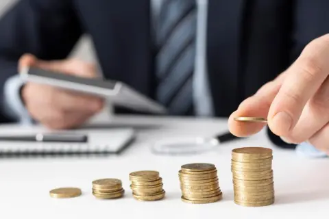 Dłoń kładzie monetę na rosnącej stercie, symbolizując zabezpieczenie alimentów i budowanie finansowej przyszłości.