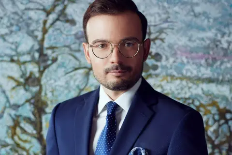 Mężczyzna w okularach i granatowym garniturze na tle abstrakcyjnego obrazu.