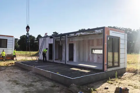 Budowa modułowego budynku, zgodna z art. 29 prawa budowlanego. Dźwig podnosi element konstrukcyjny.