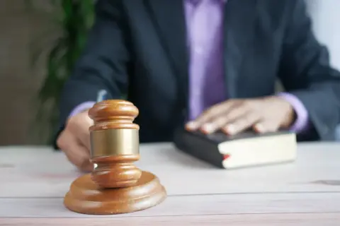 Sędzia kładzie rękę na księdze podczas rozprawy sądowej. Obok stoi drewniany młotek.
