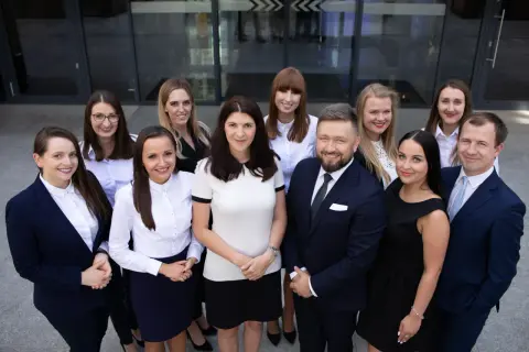 Grupa prawników w garniturach i strojach biznesowych pozuje przed budynkiem.