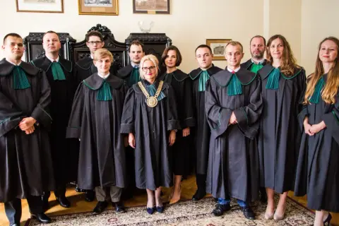 Grupa prawników w togach stoi w pomieszczeniu.