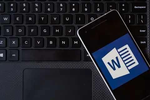 Smartfon z ikoną Worda leży na klawiaturze. Możesz kliknąć ten hiperłącze, aby otworzyć dokument.
