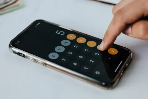 Dłoń wpisuje liczby na kalkulatorze w telefonie. Obliczenia mogą dotyczyć darowizny a zachowek.