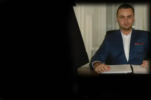 Mężczyzna w niebieskiej marynarce siedzi przy biurku z dokumentami.