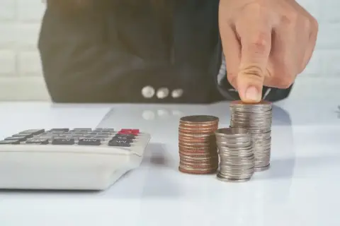 Ręka układa monety na stosie, obok kalkulatora. Zastanawiasz się, ile kosztuje sprawa o zasiedzenie u adwokata?