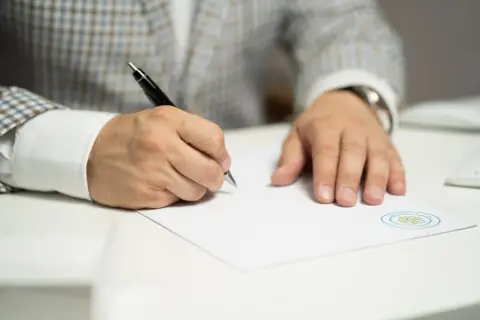 Mężczyzna w eleganckiej marynarce podpisuje dokument. To ważny odpis wyroku rozwodowego, który kończy pewien etap życia.
