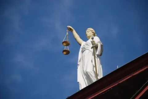 Posąg Temidy z wagą i mieczem na tle błękitnego nieba.
