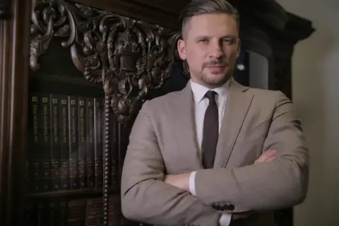 Mężczyzna w garniturze stoi przed regałem z książkami.