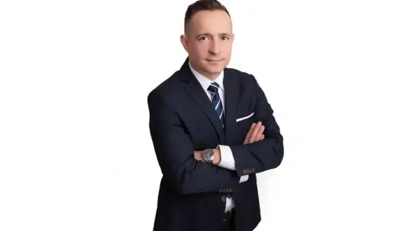 Mężczyzna w garniturze ze skrzyżowanymi rękami na białym tle.