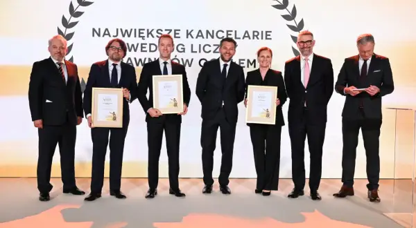 Sześć osób w garniturach odbiera nagrody na scenie.